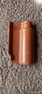 Telha cerâmica em tom terracota, modelo curvo típico de telhas intertravadas, posicionada sobre superfície de concreto rugoso. O objeto apresenta inscrições em relevo com informações de fabricante e origem: “TONAL INDUSTRIAS TONAL S.A. DE C.V. HECHO EN MEXICO NOM-141-SEMARNAT-2003 P3 ALBERCA 31-131300”. A peça está íntegra e em bom estado.