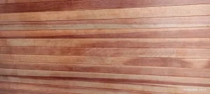 Estrutura de parede composta por tábuas de madeira dispostas horizontalmente, em diferentes tonalidades de marrom e avermelhado, com veios naturais visíveis que destacam a textura e o acabamento rústico. As peças estão alinhadas de forma uniforme, criando padrão contínuo