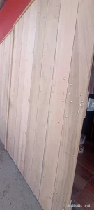 Portão de madeira clara composta por pranchas verticais fixadas com parafusos